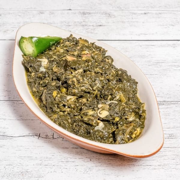 A white oval dish filled with dark green, stewed spinach, garnished with a lime wedge.