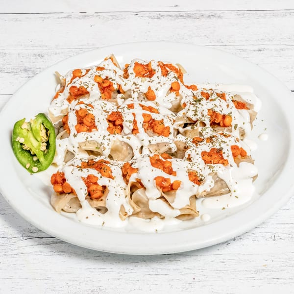 DeAfghanan Cuisine's Mantu dumplings topped with white sauce, orange lentils, and dried herbs, with a jalapeño.