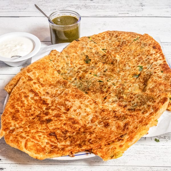 Golden-brown Afghan Bolani flatbread, cut into squares, served with green chutney and white yogurt sauce.