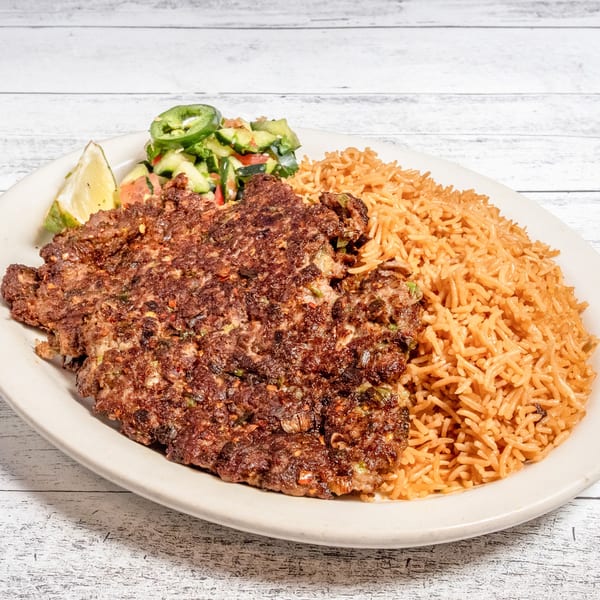 Chapli Kabob with seasoned rice, a side salad with jalapeños, and lime wedges on a white plate.