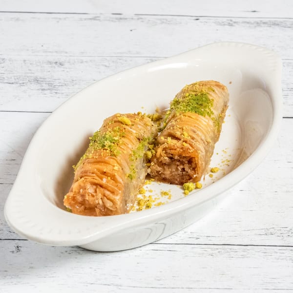 Two pieces of Afghan baklava, sprinkled with green pistachios, served in a white dish.
